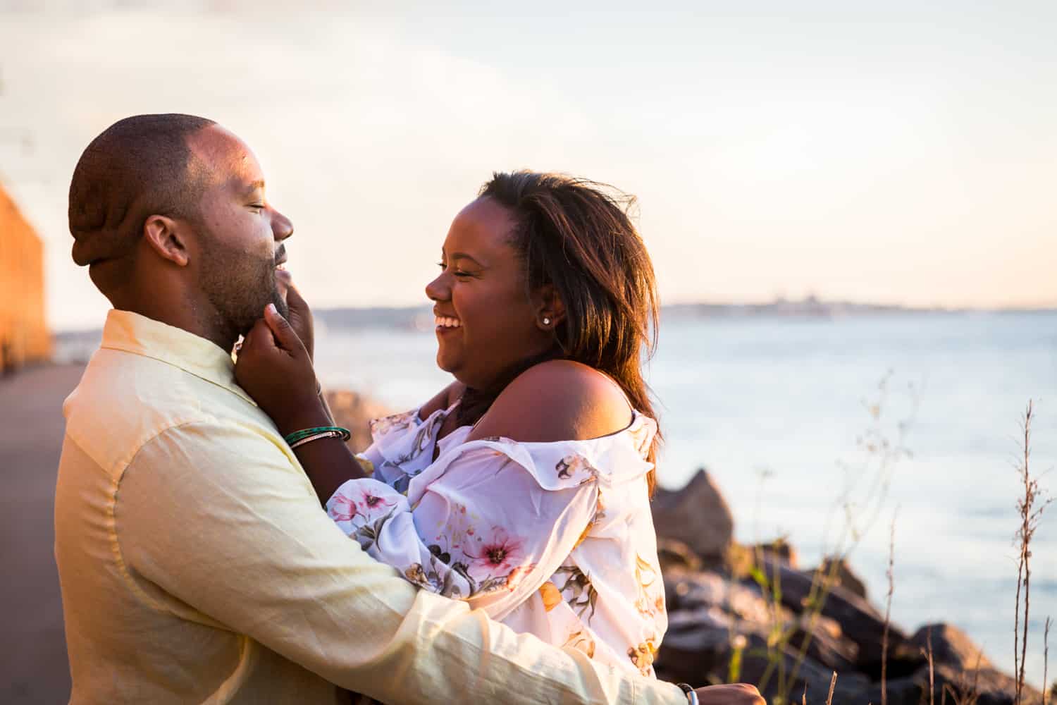 African American couple hugging in front of NYC waterfront for an article on creative engagement photo shoot ideas