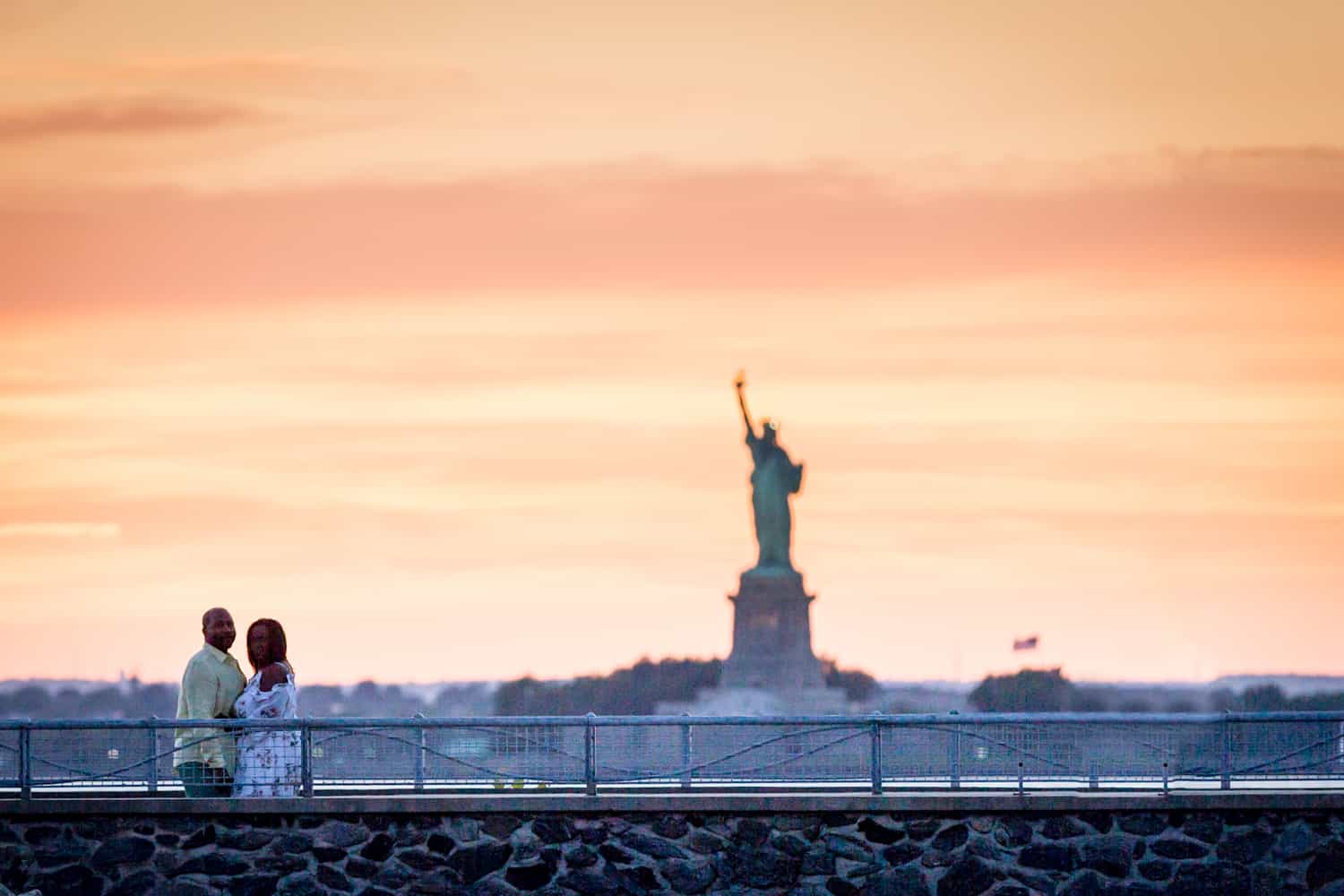Couple on dock with Statue of Liberty in background at sunset