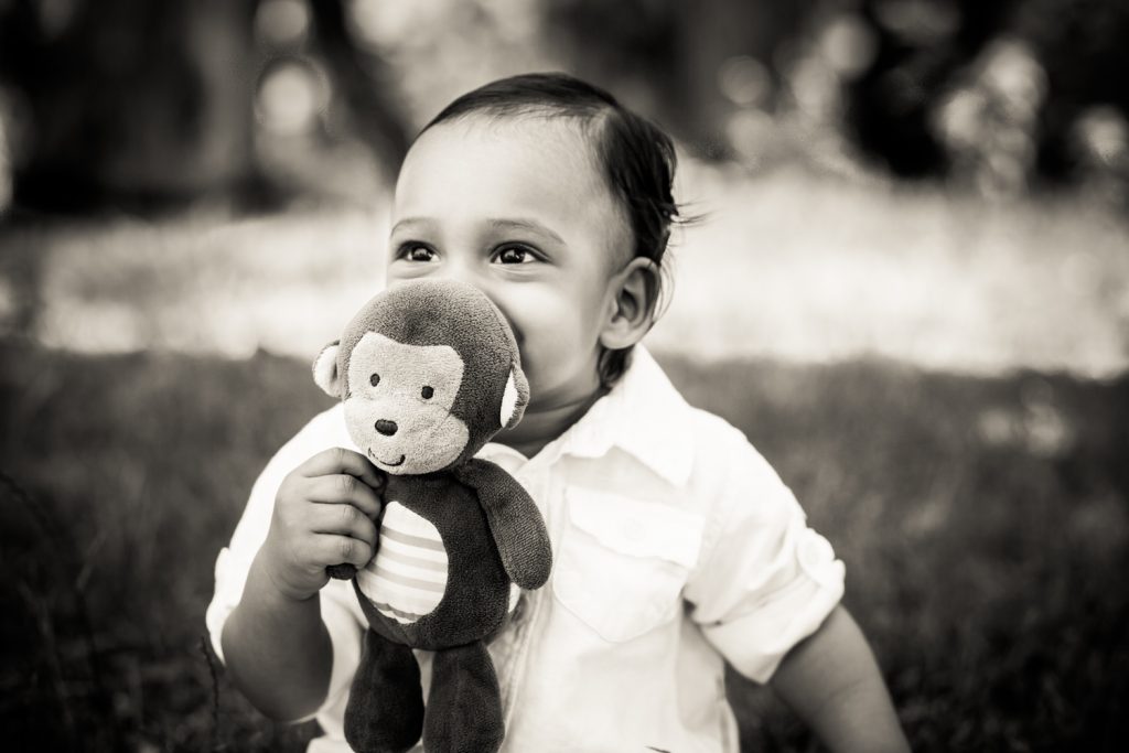 Black and white photo of baby chewing on stuffed toy monkey