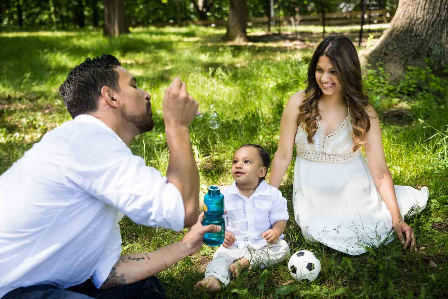 Parents sitting in grass and blowing bubbles with son