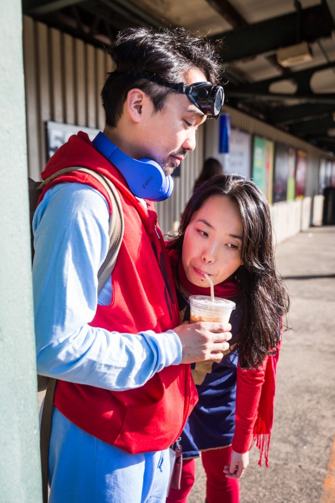 Couple sipping from a cup dressed as Spiderman and Supergirl for a Comic Con engagement shoot