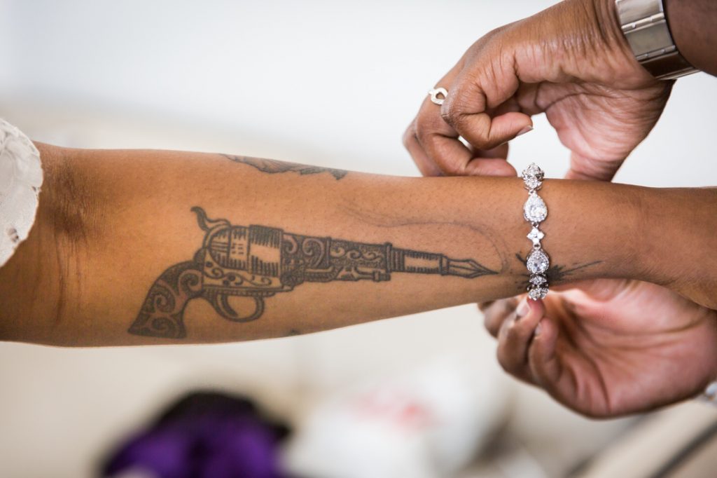 Bride with arm tattoo putting on bracelet for an article on elopement tips