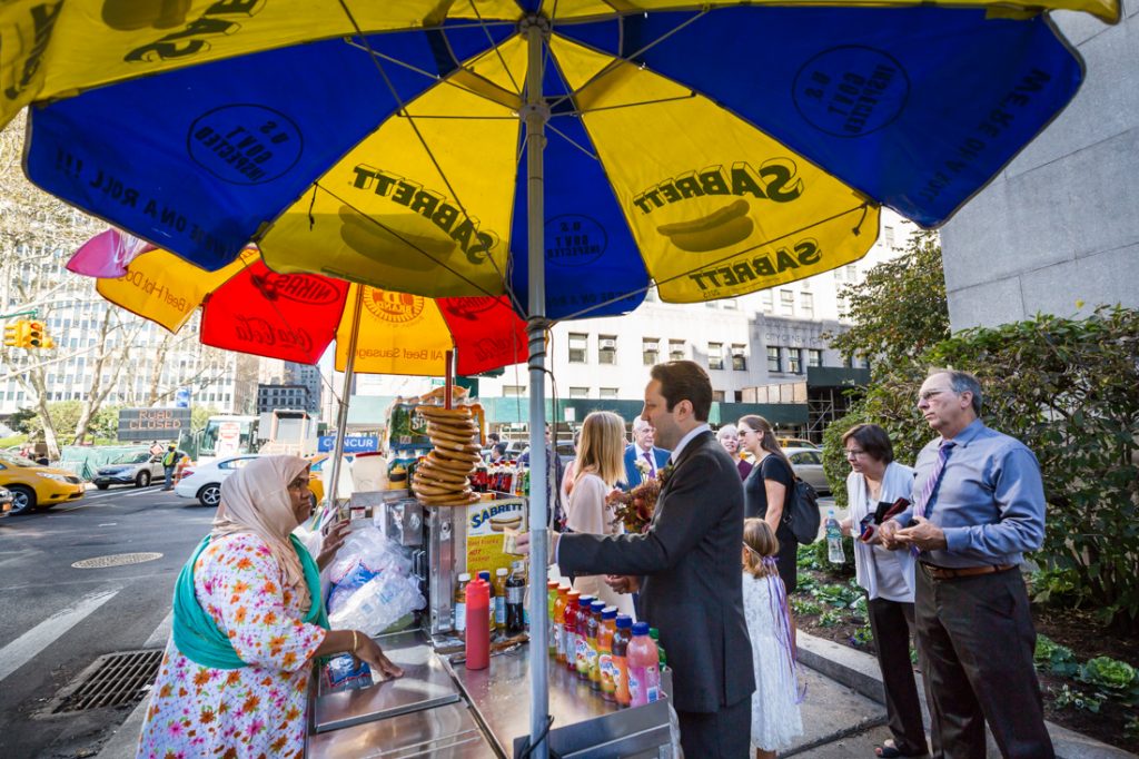 Groom buying water at a hot dog stand for an article on How to Get Married at City Hall in Any NYC Borough