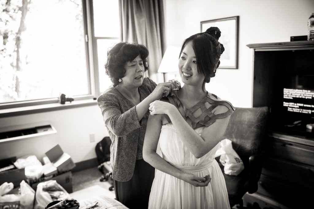 Black and white photo of mother attaching cape to bride at a Bear Mountain Inn wedding