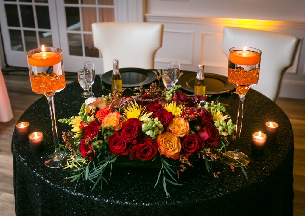 Sweetheart table setting with orange flower centerpiece and candles for an article on how to plan a Halloween wedding