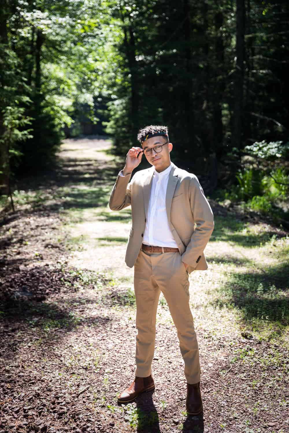 Young man wearing tan suit and touching glasses in woods