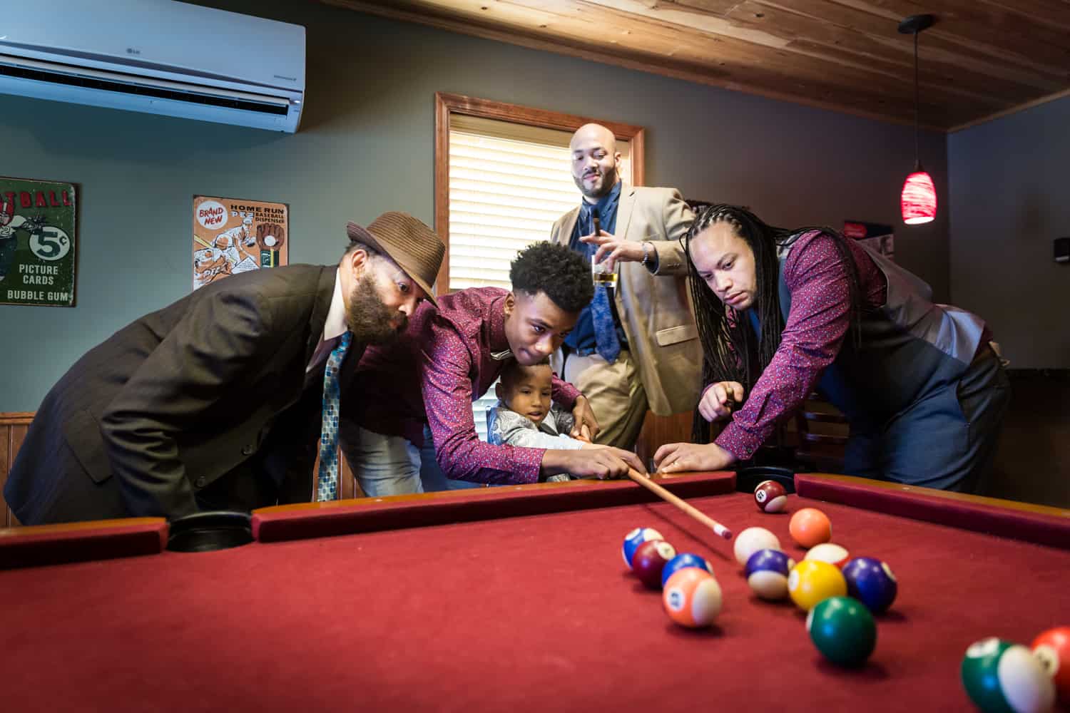 Male family members helping a little boy play pool during a family reunion portrait