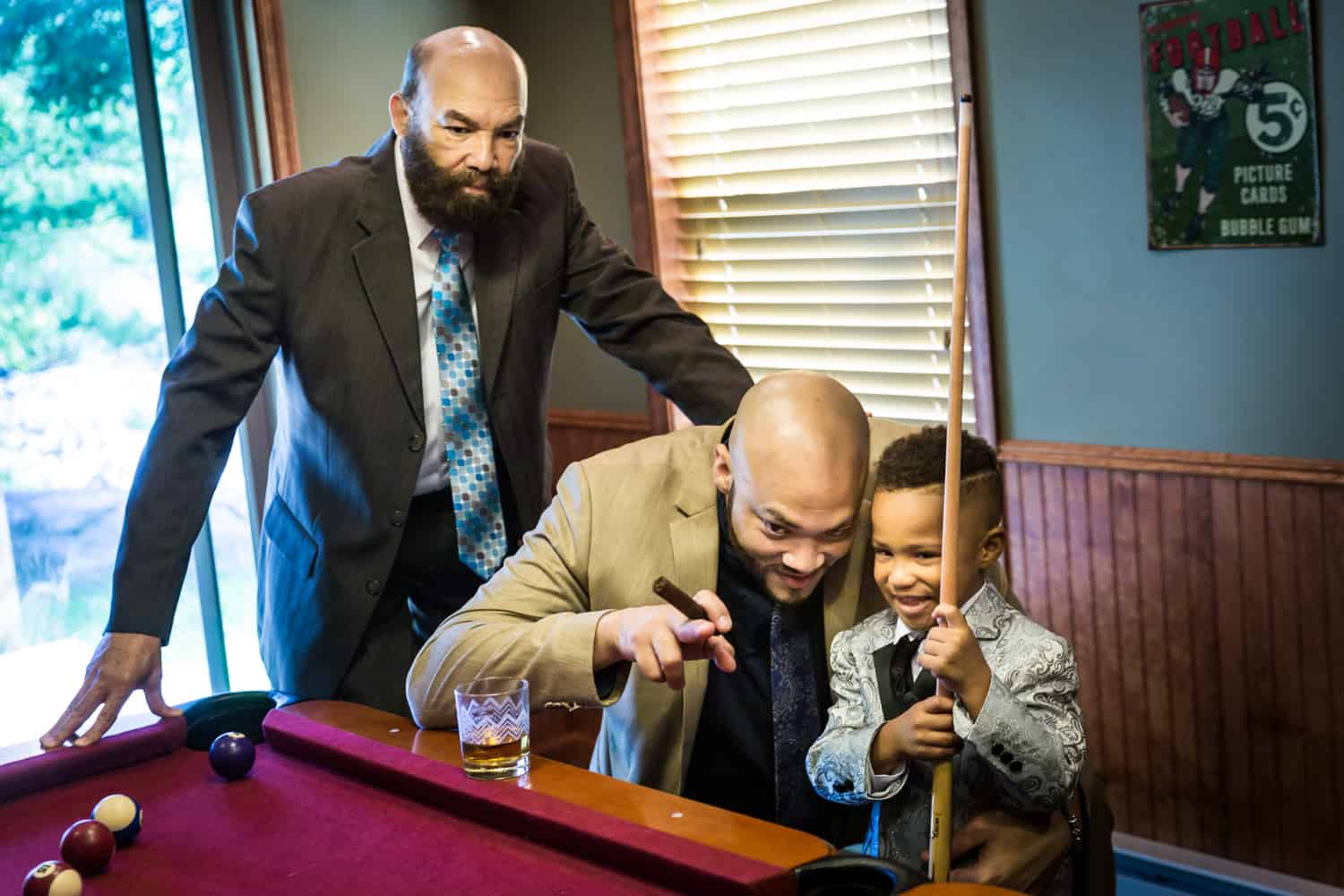 Two male family members helping little boy play pool during a family reunion portrait