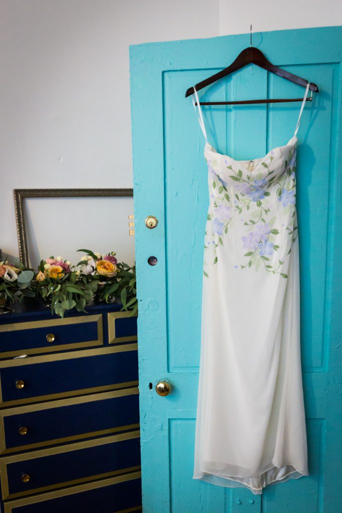 White, floral wedding dress hanging on blue door for an article on the pros and cons of a restaurant wedding