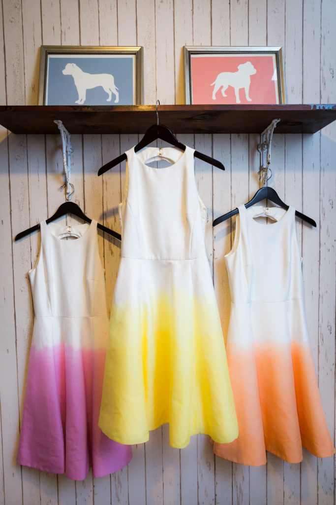 Three brightly colored, ombre bridesmaids dresses hanging from shelf for an article on the pros and cons of a restaurant wedding