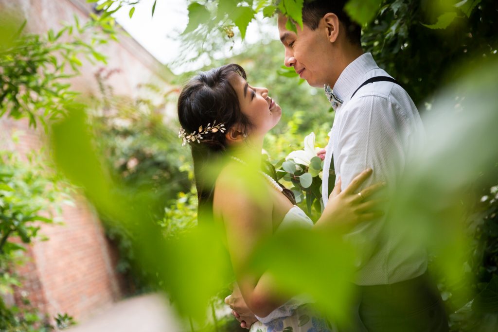 View through leaves of bride and groom looking at each other for an article on the pros and cons of a restaurant wedding