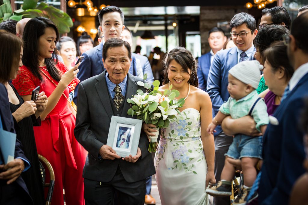 Bride and father walking down aisle with photo of mother at restaurant wedding ceremony