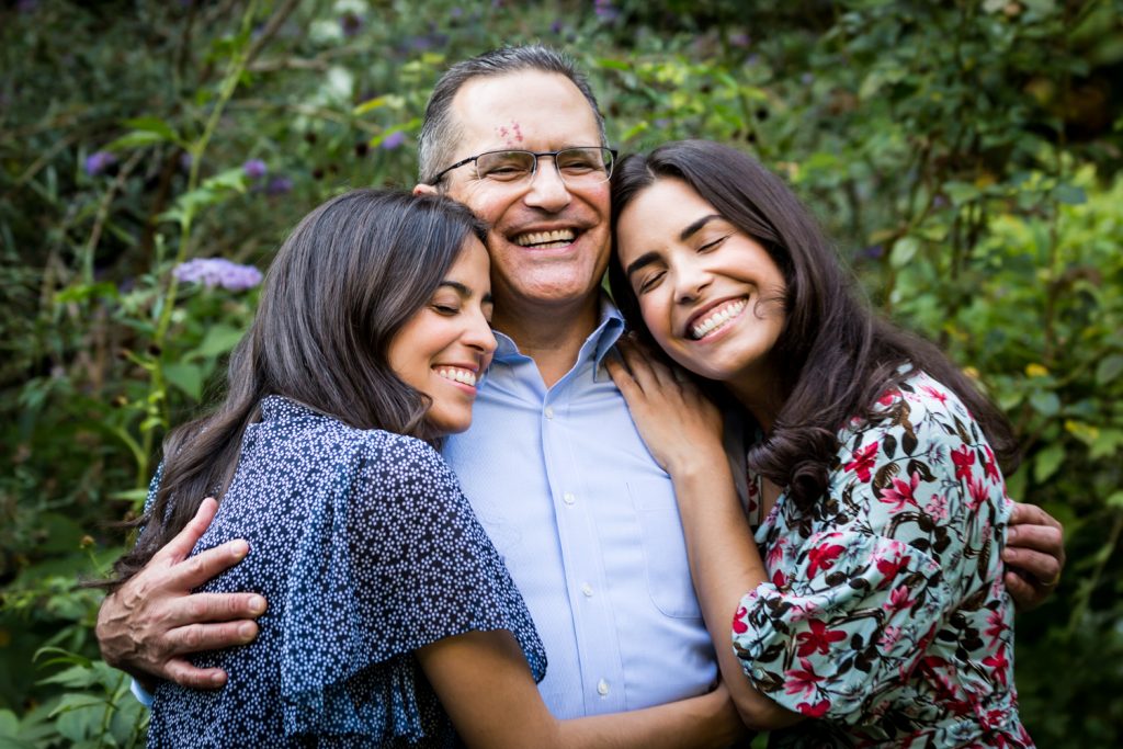 Father and two women hugging in middle of garden at a community garden family portrait session