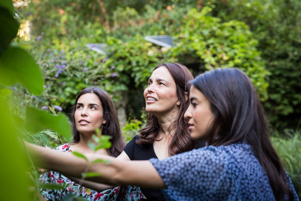Woman showing plants to two daughters in middle of garden
