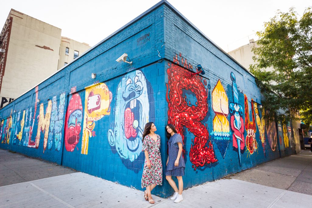 Two sisters standing against corner of colorful mural in East Village