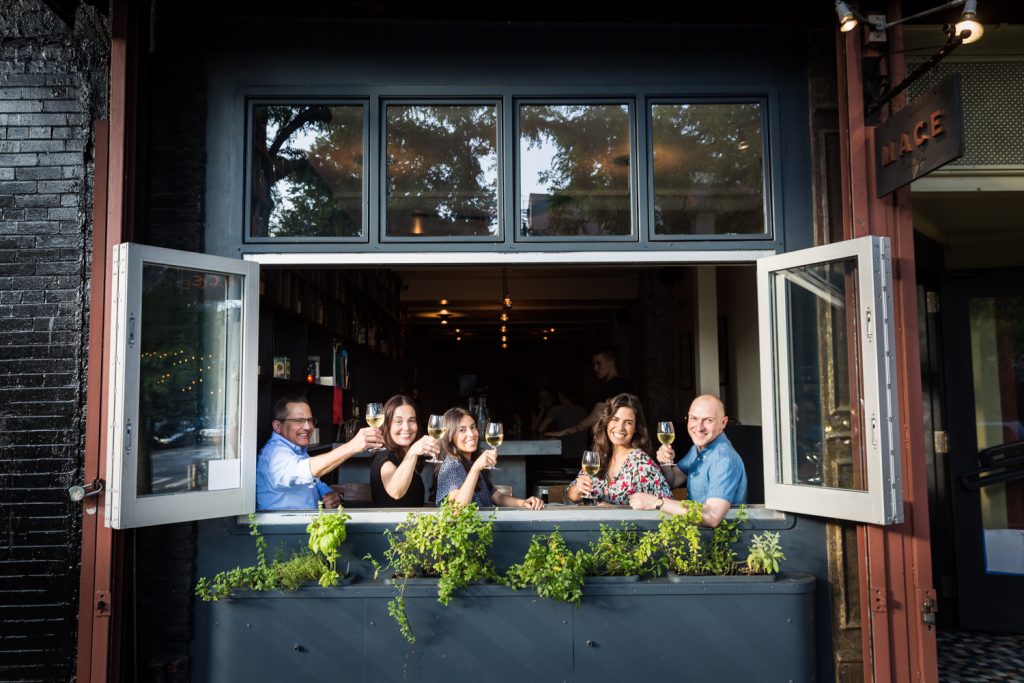 Family raising glasses of wine through window of wine bar