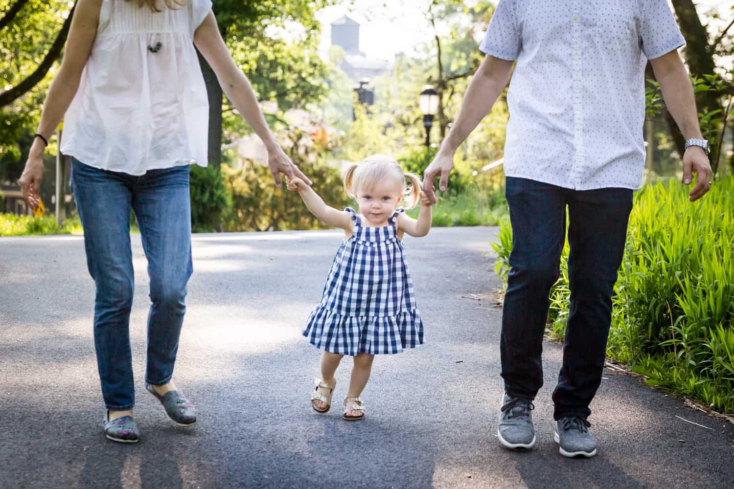 Little girl holding hands of parents in Forest Park for an article on toddler portrait tips