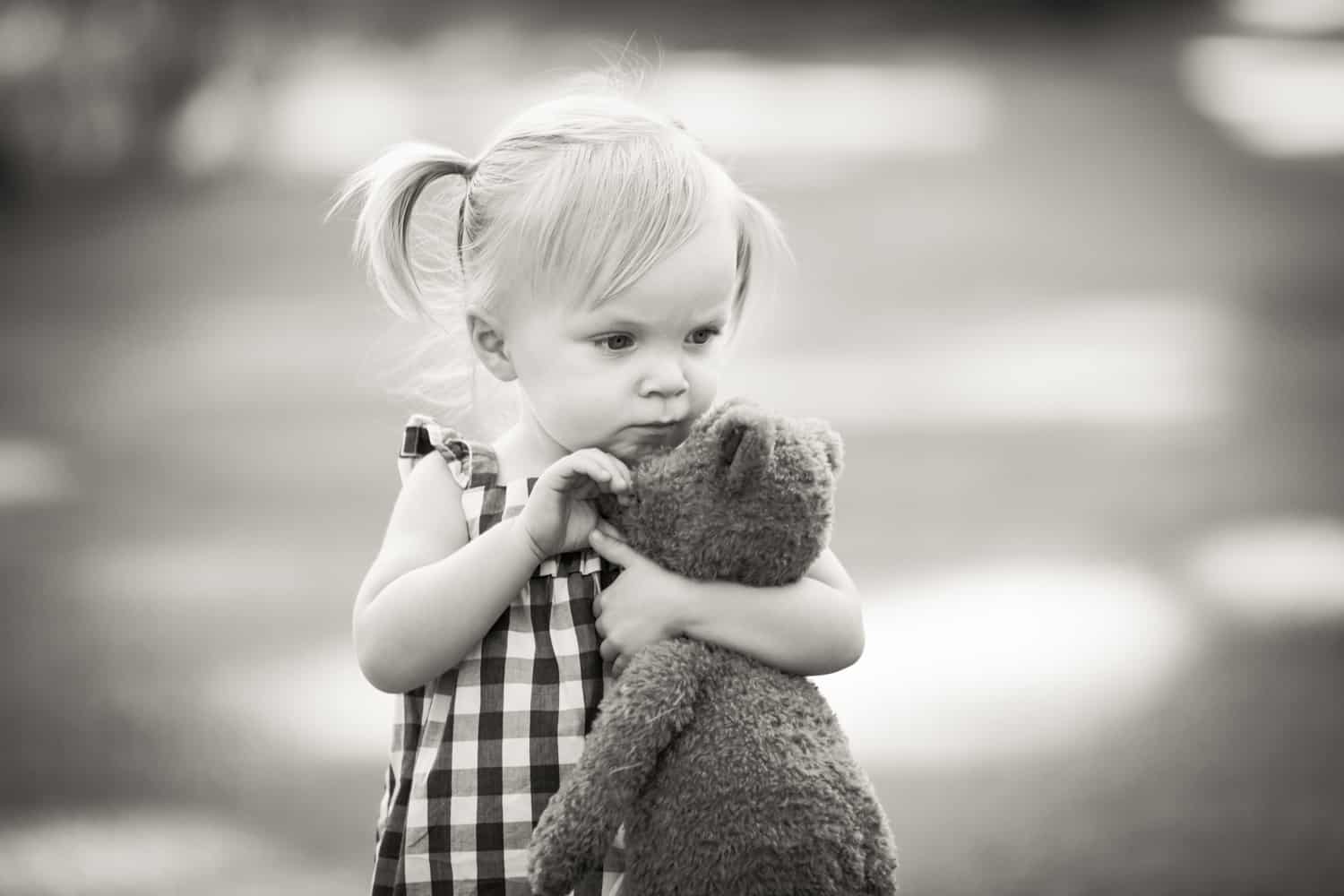 Black and white photo of little girl holding stuffed teddy bear