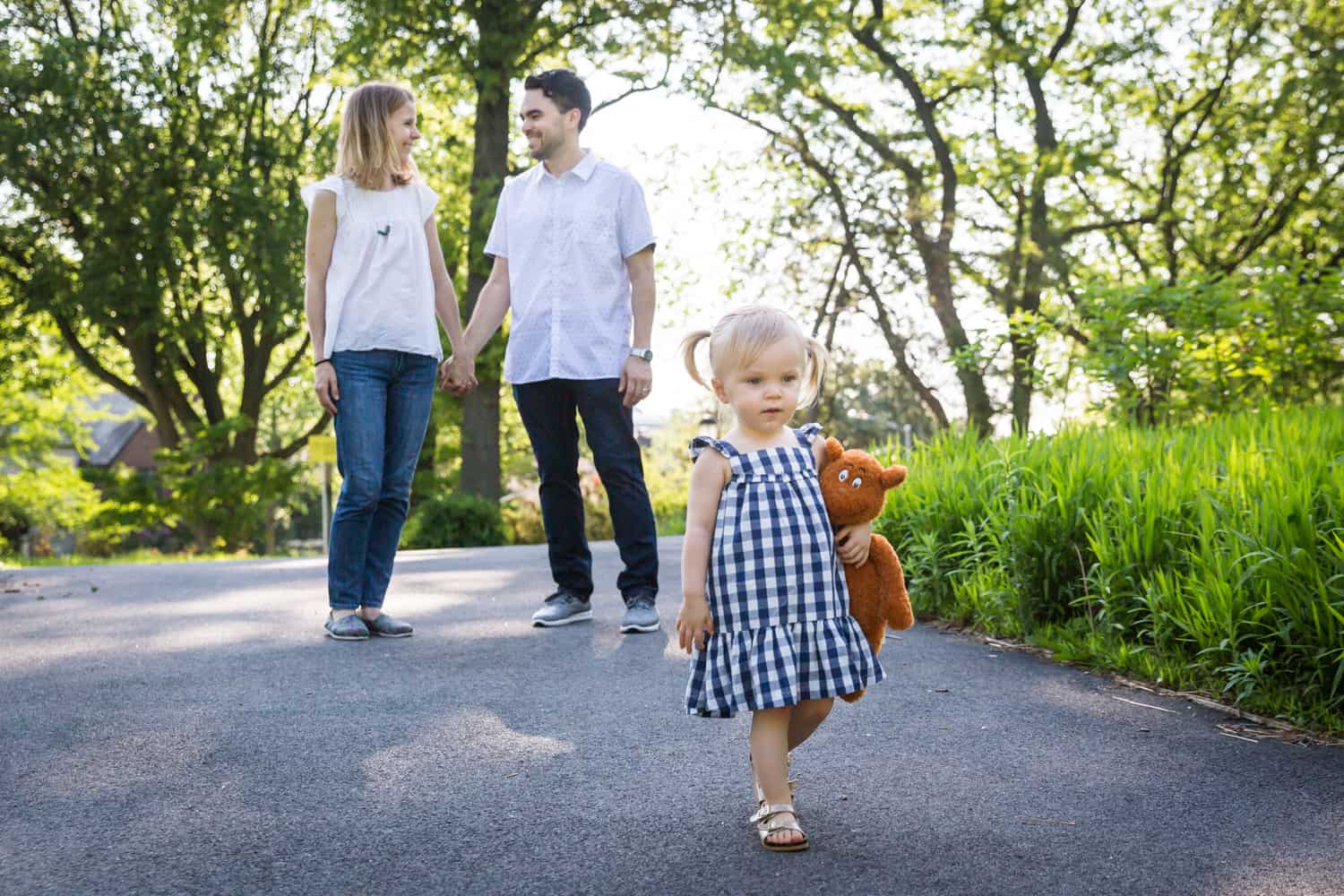 Parents holding hands behind little girl wearing blue checked dress