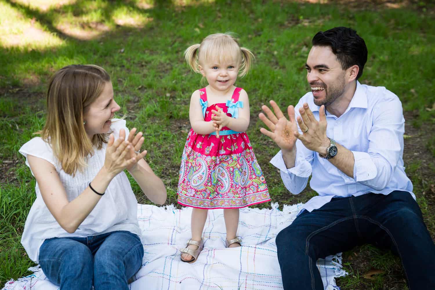 Parents clapping with little girl on blanket during a Forest Park family photo shoot