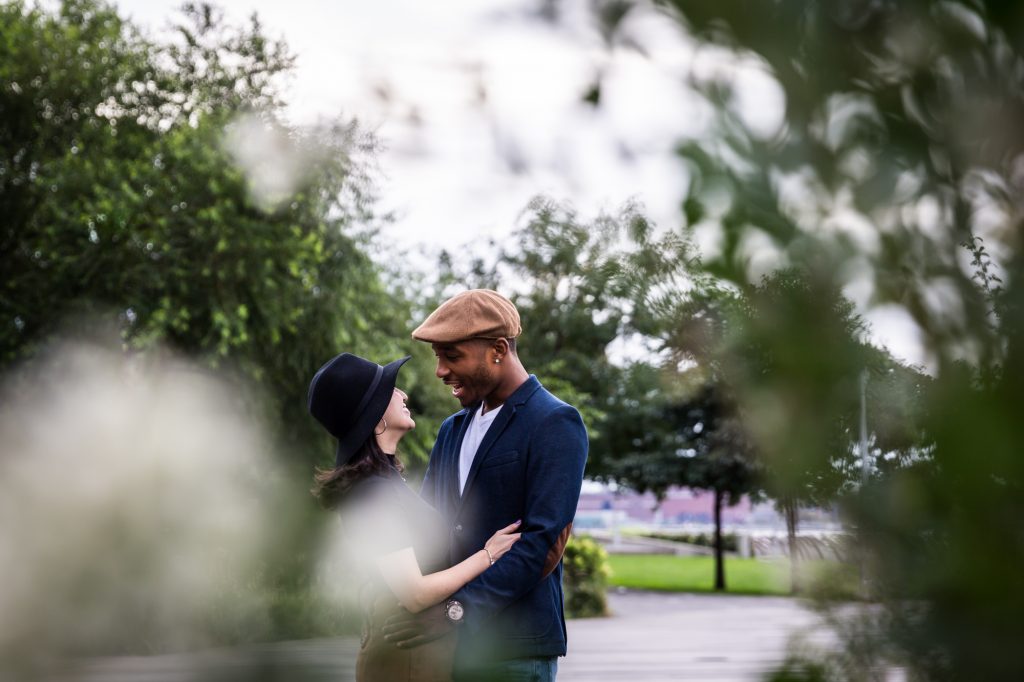 View through leaves of couple hugging during Long Island City engagement shoot