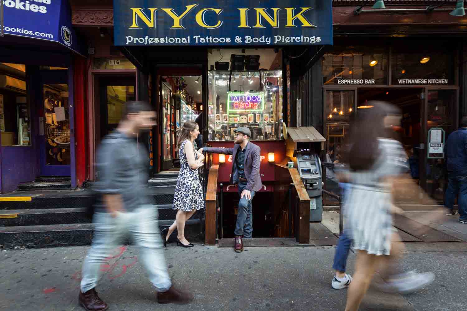 Couple in front of tattoo shop with people walking past in a blur for a Greenwich Village engagement portrait