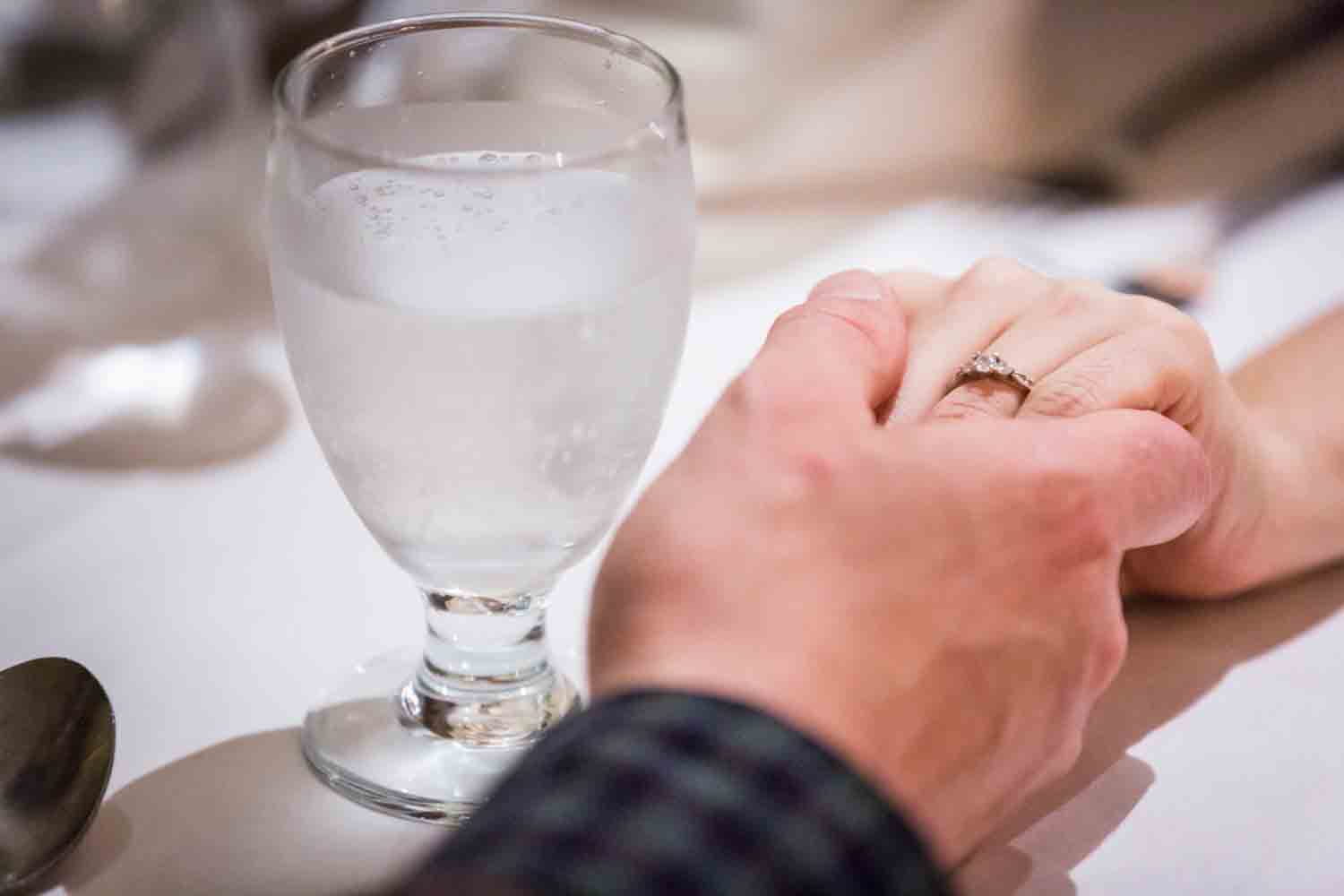 Close up on couple holding hands at table with woman wearing engagement ring