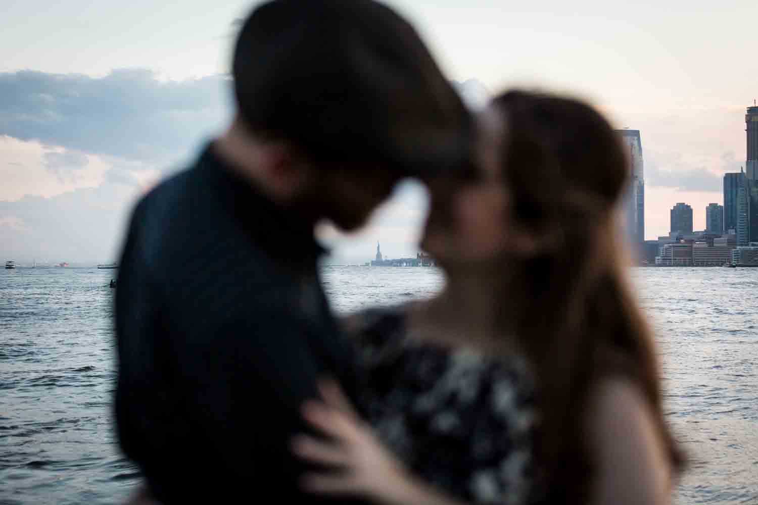 Couple out of focus kissing with Statue of Liberty in background