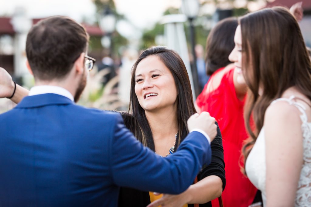 Female guest reaching to hug groom during cocktail hour