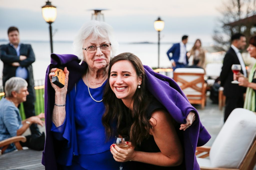 Older woman and younger woman under one purple coat at cocktail hour