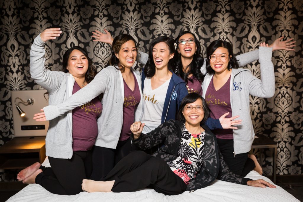 Bride, bridesmaids, and mother of the bride cheering on a bed at a Westbury Manor wedding
