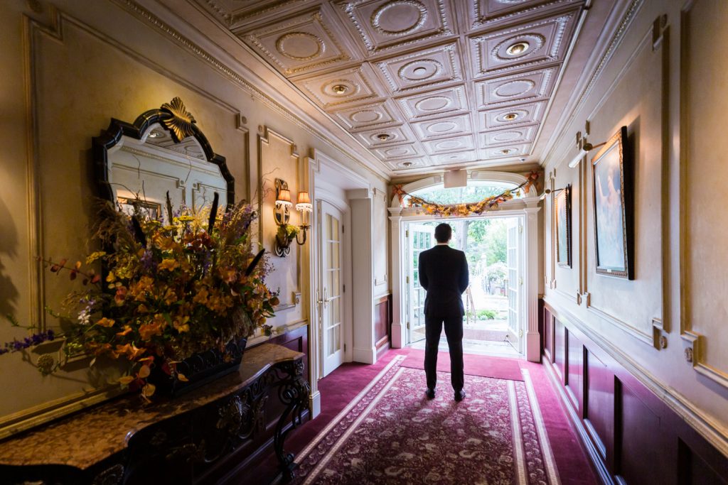Groom standing at end of hall waiting for first look to begin at a Westbury Manor wedding