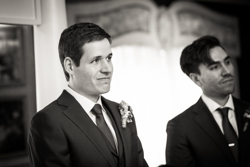 Black and white photo of groom waiting for bride at ceremony