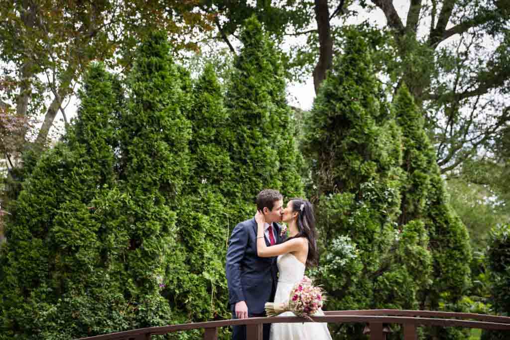 Bride and groom kissing on bridge in garden at a Westbury Manor wedding