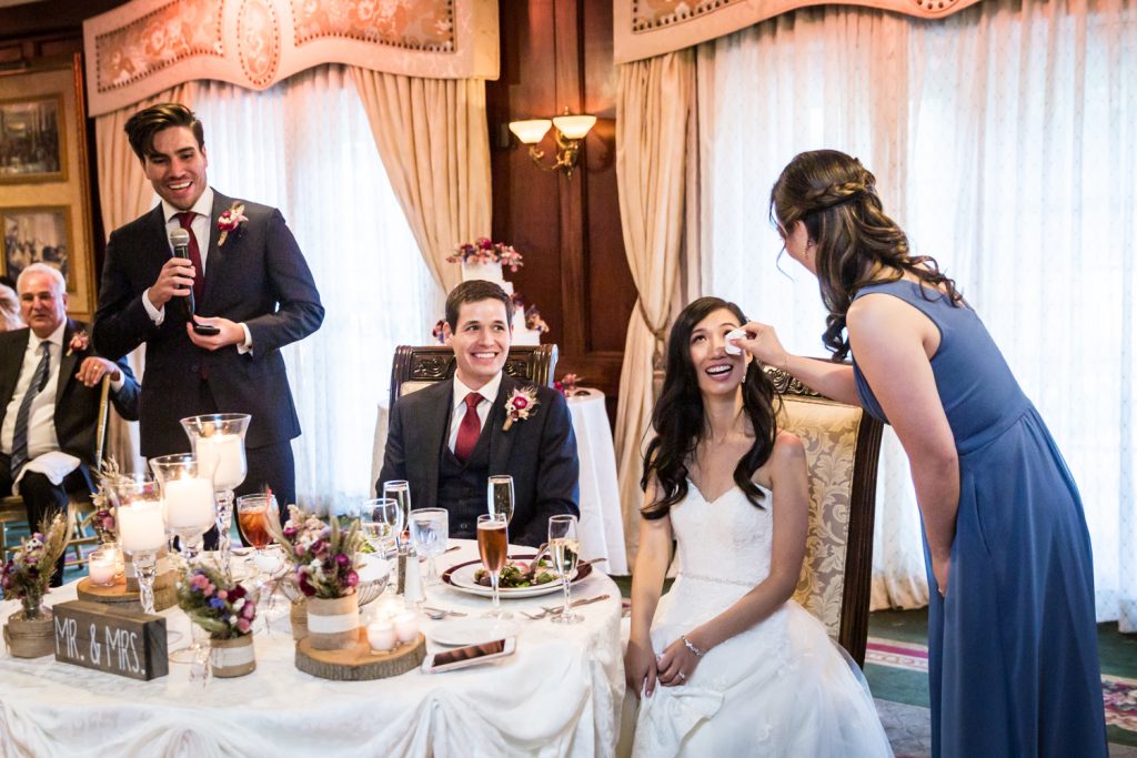Maid of honor wiping tears from bride's face during speech