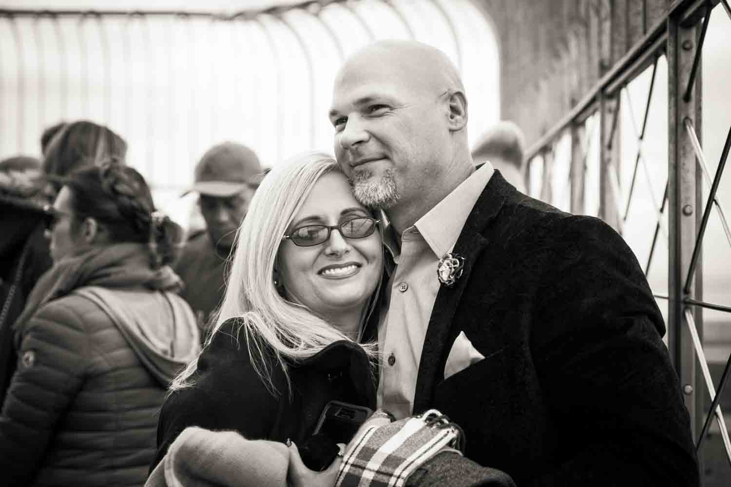 Black and white photo of couple hugging at top of Empire State Building