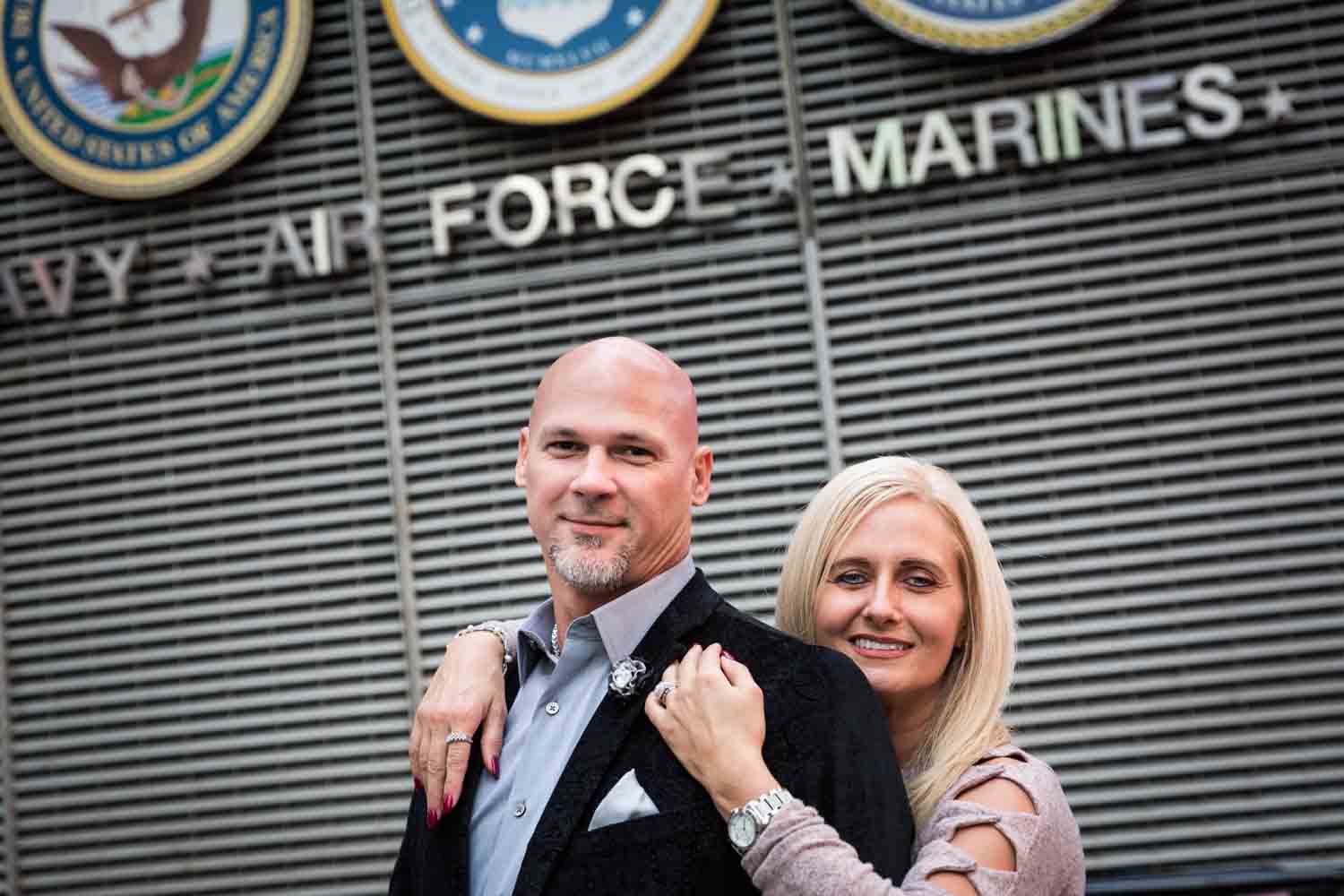 Woman hugging man from behind in front of military sign for an article on how to propose on top of the Empire State Building