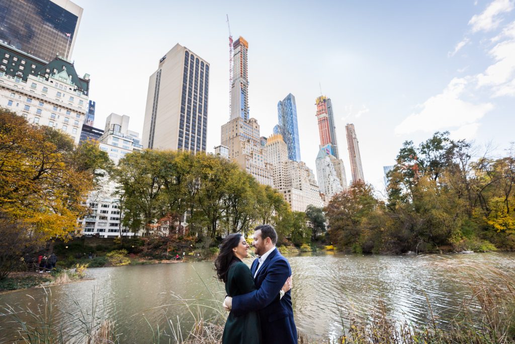 Couple hugging in Central Park with lake and NYC skyline in background for an article on winter portrait tips