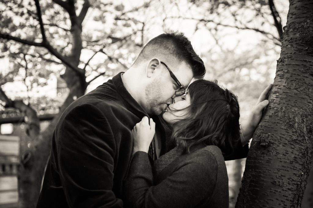 Black and white photo of couple kissing underneath cherry blossom trees