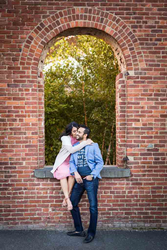 Pregnant woman kissing her husband's cheek in brick archway for article on maternity portrait tips