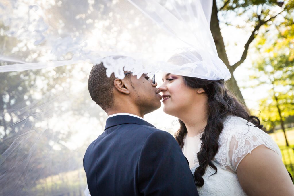 Bride and groom underneath blowing veil