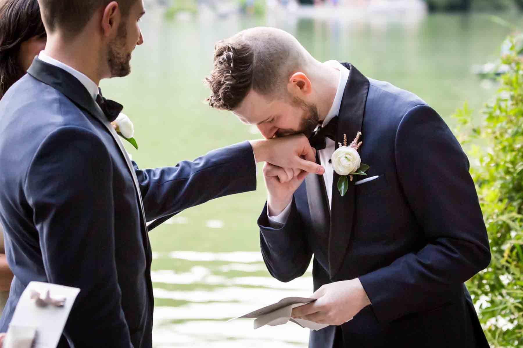 Groom kissing groom's hand for an article entitled, ‘Do you need a permit to get married in Central Park?’