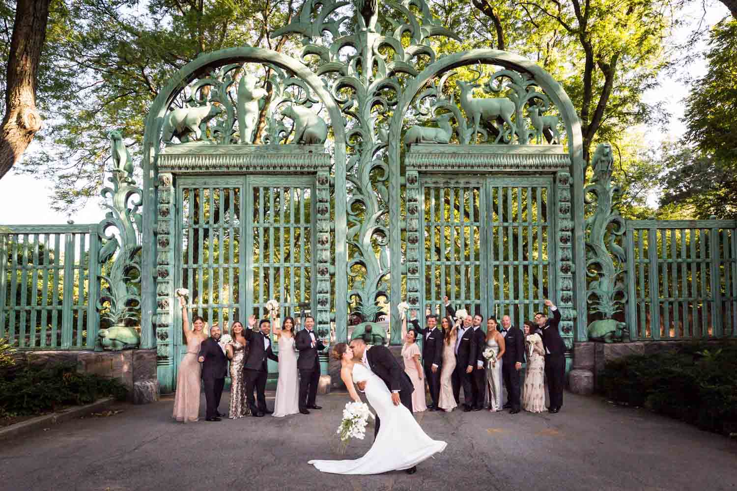 Bride and groom kissing in front of bridal party and Southern Boulevard gates for an article on Bronx Zoo wedding venue updates