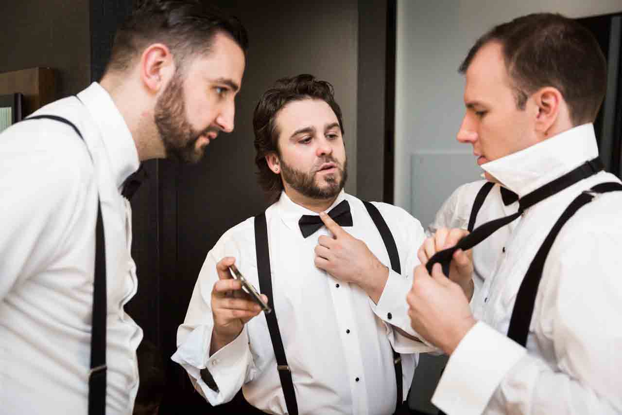Groom and groomsmen trying to tie bowtie at a Central Park Conservatory Garden wedding