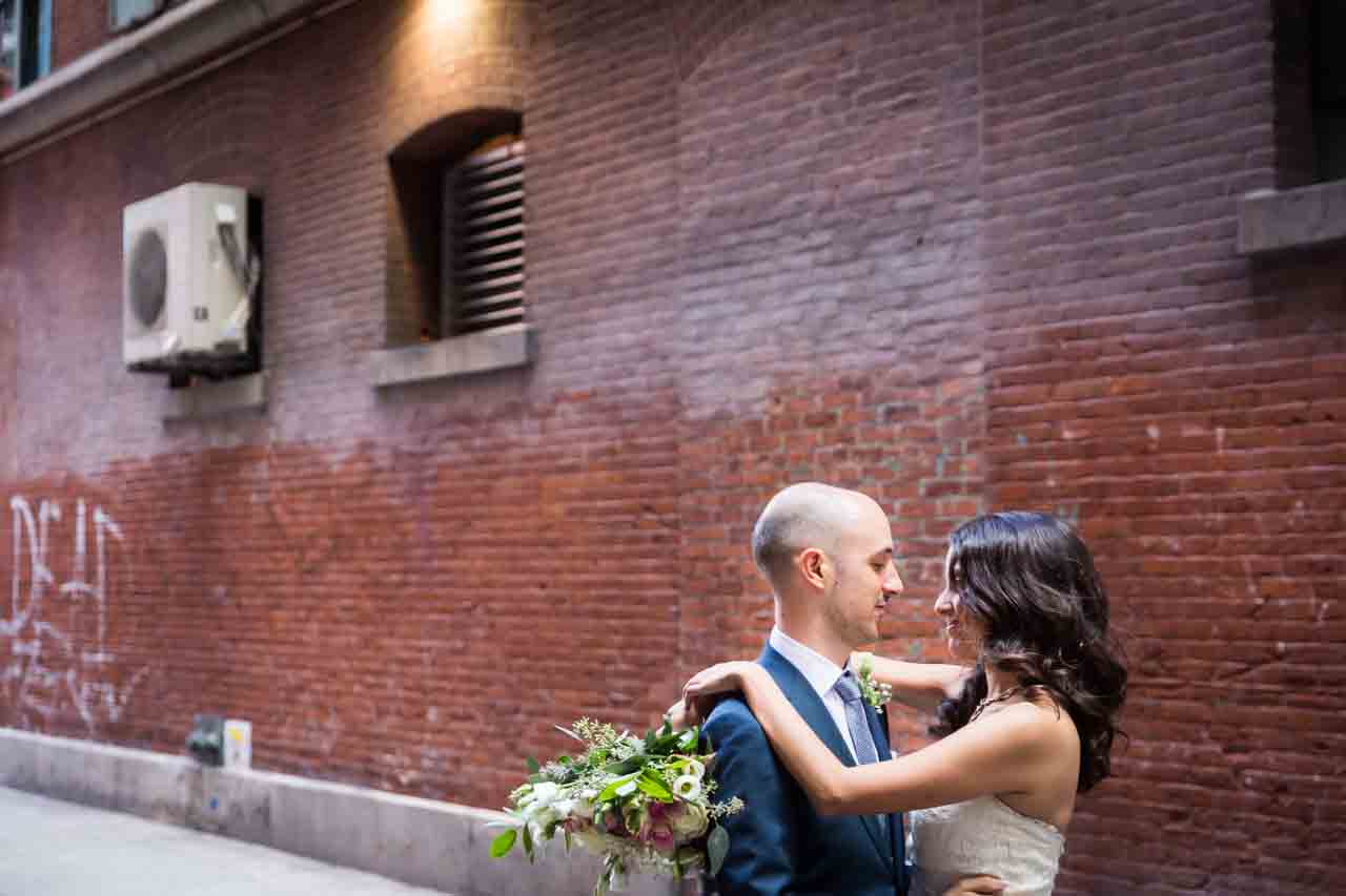 Bride and groom hugging in brick alleyway for an article on non-floral centerpiece ideas