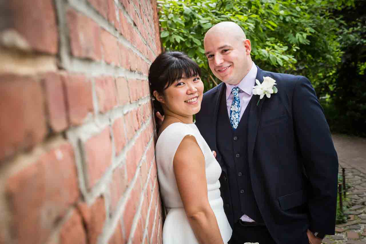 Bride and groom looking into camera against brick wall