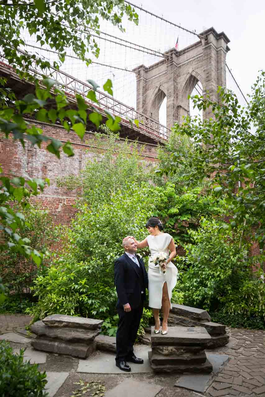 Bride standing on stone steps with groom in Brooklyn Bridge Park