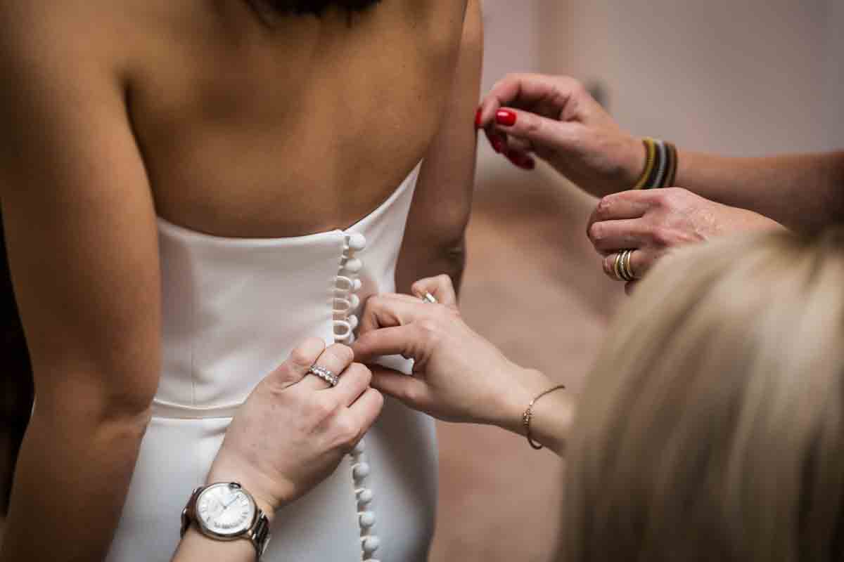 Hands closing buttons on a bride's wedding dress