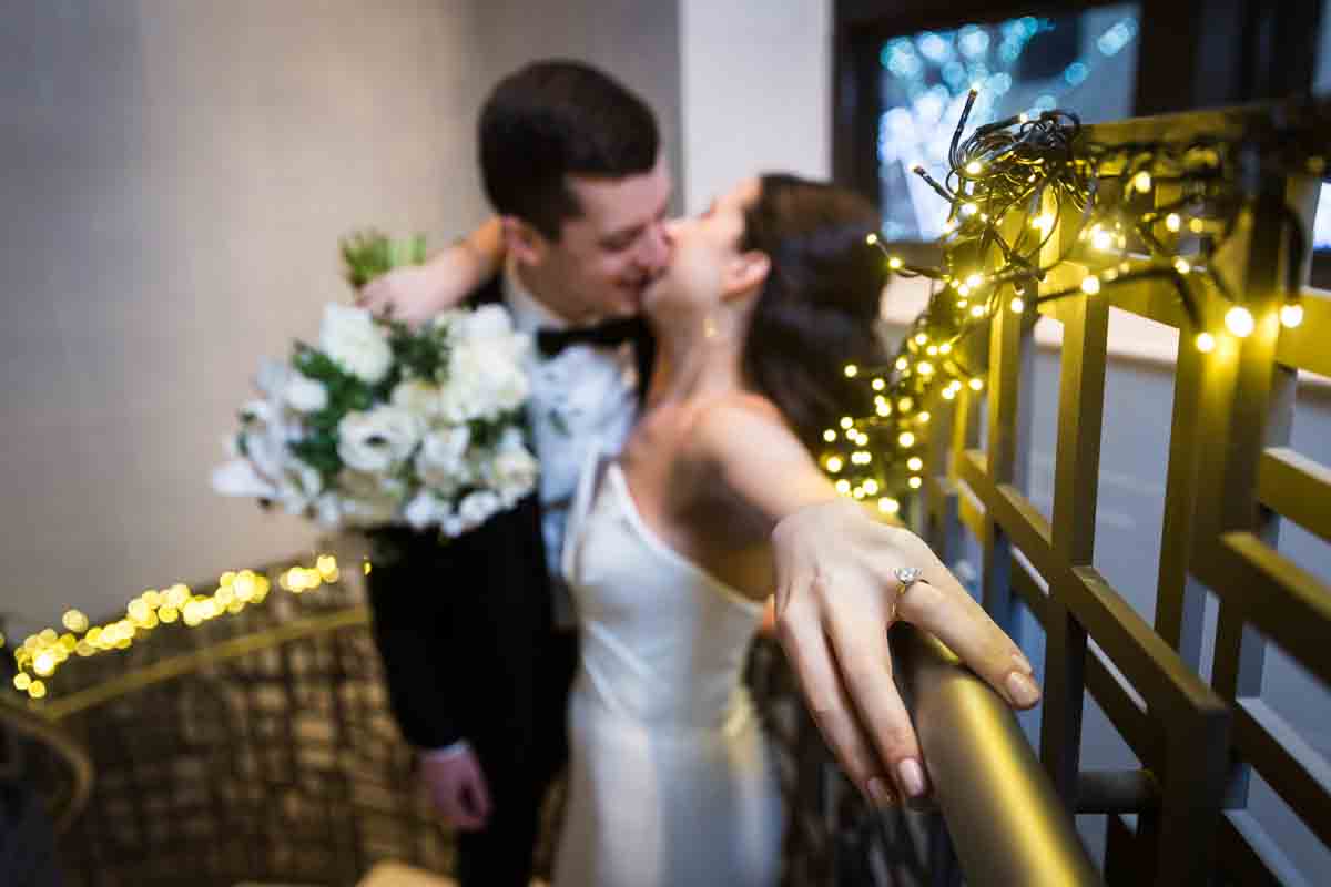 Outstretched hand of bride in front of bride and groom kissing