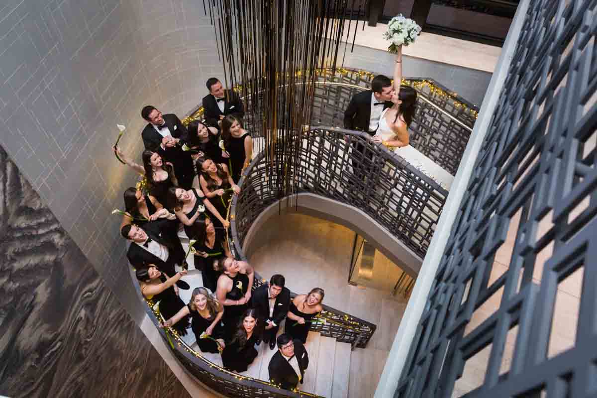 Bridal party celebrating as bride and groom kiss on the Four Seasons Hotel New York Downtown staircase